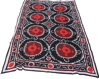 May include: A large, rectangular textile with a black background and a repeating pattern of red and white floral designs. The border features a similar floral motif. The textile is likely used as a decorative element, such as a wall hanging or a bedspread.