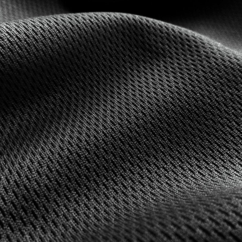 May include: Close-up of a black, textured fabric with a grid pattern. The fabric is soft and flexible, and it has a slightly shiny finish.