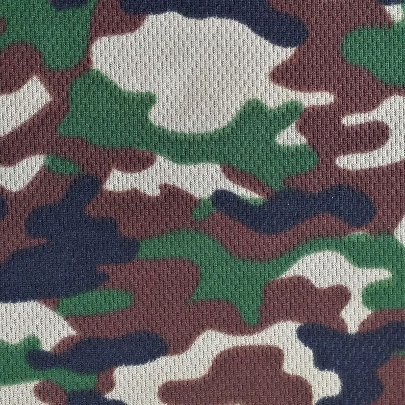 May include: Camouflage fabric with a textured, woven pattern. The fabric features a mix of green, brown, black, and white colors in a classic camouflage design.