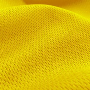 May include: Close-up of a bright yellow fabric with a textured, mesh-like pattern. The fabric is soft and flexible, with a slightly wrinkled appearance.