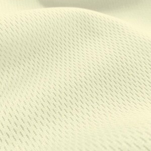 May include: Close-up of a cream-colored fabric with a textured, woven pattern. The fabric has a subtle sheen and a soft, smooth feel.