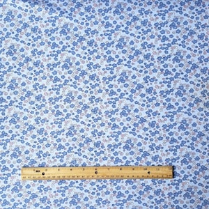 May include: A close-up of a blue fabric with a white and pink floral pattern. A ruler is placed on the fabric to show the scale.