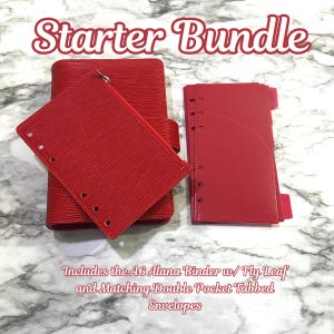 May include: A red starter bundle set including an A6 Alana binder, a zippered pouch, and double pocket tabbed envelopes. The set is displayed on a marble-patterned surface. The text "Starter Bundle" is at the top.