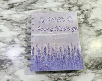 May include: A purple and white spiral bound notebook with a lavender field design and glitter. The text "$10,000 Saving Challenge" is printed on the front cover.