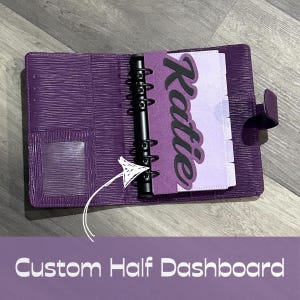 May include: A purple A6 binder with a textured exterior, featuring a black six-ring metal mechanism. Inside, a custom purple half-dashboard displays the name Katie in black script lettering, accompanied by light purple tabbed dividers.