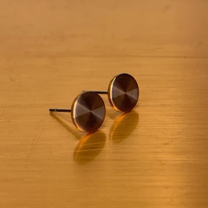 May include: A pair of round, gold-toned stud earrings with a subtle, textured finish.