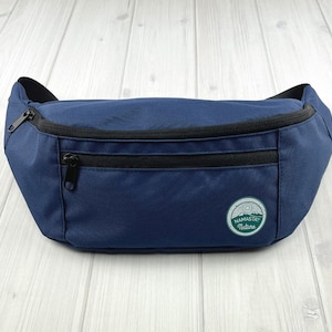 May include: A dark blue fanny pack with a black zipper and a green and white patch that says "Namaste Nature".