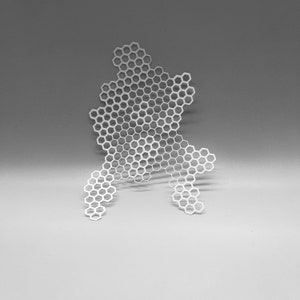 May include: A white, honeycomb-patterned decorative object. The object is made up of numerous hexagonal shapes, creating an open design. The overall shape is irregular, with a flowing, organic form. It is set against a grey background.