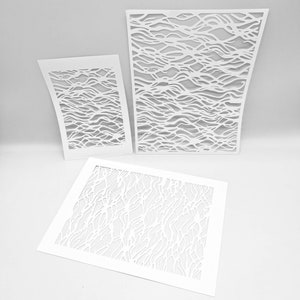 Puede incluir: Tres recortes de papel blanco con un patrón ondulado orgánico. Los recortes son de diferentes tamaños y están dispuestos sobre una superficie blanca.