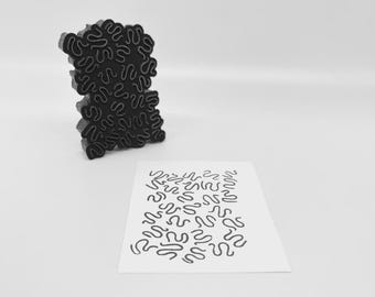 Könnte beinhalten: Ein schwarzer, abstrakter Stempel mit einem wellenförmigen Muster, neben einer weißen Karte mit dem gestempelten Design. Der Stempel ist ein fester, dreidimensionaler Gegenstand. Die Karte zeigt das Design des Stempels in schwarzer Tinte.