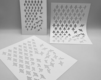 Könnte beinhalten: Drei weiße Schablonen mit ausgeschnittenen Designs. Zwei Schablonen sind rechteckig, eine ist quadratisch. Die Schablonen weisen ein sich wiederholendes Muster aus Rauten und stilisierten Vogelformen auf. Die Schablonen sind auf einer hellgrauen Oberfläche angeordnet.
