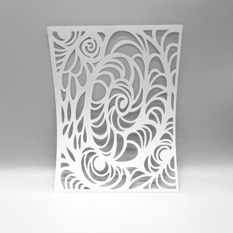 May include: A white, laser-cut decorative panel with an intricate, swirling design. The pattern features organic shapes, including spirals and flowing lines, creating a sense of movement. The panel is slightly curved, adding dimension to the design.