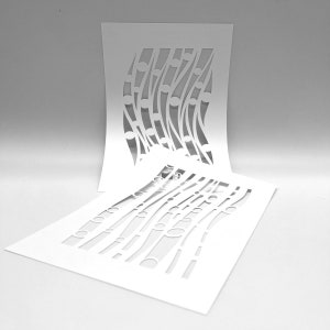 May include: Two white paper stencils with a flowing, abstract design. The stencils feature curved lines and circular cutouts, creating a pattern. One stencil is upright, while the other lies flat, showcasing the design.