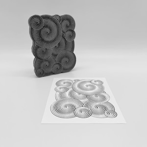 May include: A black and gray stamp with a pattern of concentric circles, next to a print of the same design on white paper. The stamp is three-dimensional, with the circles at varying heights. The print shows the stamped design.