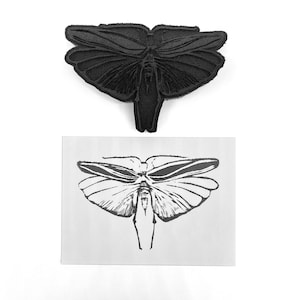 May include: A black rubber stamp of a butterfly with detailed wings and a body. The stamp is shown next to a printed image of the butterfly.