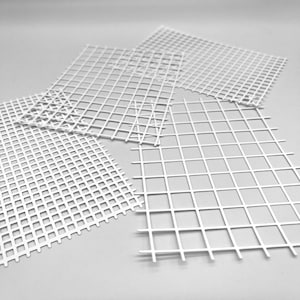 May include: Several white plastic canvas sheets arranged on a light grey surface. Each sheet features a grid pattern of evenly spaced squares. The sheets vary in size and are slightly overlapping, creating a layered effect.