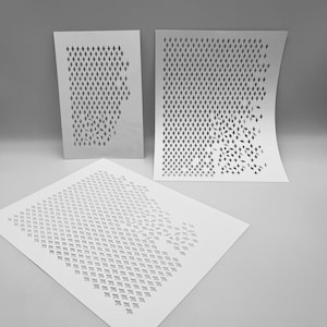 May include: Three white stencils with diamond-shaped cutouts. The stencils are arranged at different angles, with the cutouts forming a pattern that appears to be a flock of birds or a similar design. The stencils are on a light gray surface.