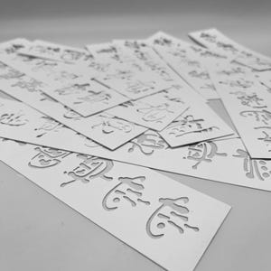 May include: A collection of white rectangular bookmarks with cut-out Chinese characters. The bookmarks are arranged in a slightly overlapping pattern, with some in focus and others blurred. The characters are stylized and intricate.