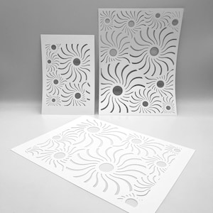 May include: Three white paper cutouts featuring a sunburst design. The cutouts are of different sizes and are arranged on a white surface. Each sunburst has a central circle with curved lines extending outwards, forming a decorative pattern.