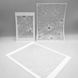 Può includere: Tre ritagli di carta bianca con un design geometrico di cerchi concentrici e linee curve. I ritagli sono rettangolari e di dimensioni variabili. Il design crea un motivo di forme circolari.