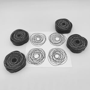Puede incluir: Sellos de arte negros y grises y diseños impresos a juego. Los sellos son circulares con un diseño en espiral. Los diseños impresos están sobre un fondo blanco. Los sellos están hechos de un material oscuro.