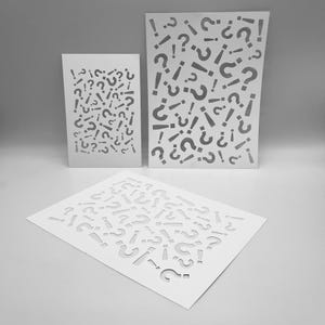 May include: Three white paper stencils featuring a repeating pattern of question marks and exclamation marks. The stencils are in varying sizes, with the largest one standing upright and the smallest one lying flat.