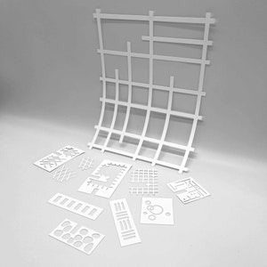 Op de afbeelding: Een set witte papiersnijwerk met geometrische ontwerpen. De ontwerpen omvatten vierkanten, cirkels en lijnen. De uitsnijdingen zijn gerangschikt op een grijs oppervlak.