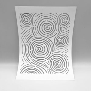 Op de afbeelding: Witte papieren uitsnede met een patroon van concentrische cirkels en gebogen lijnen. Het ontwerp cre&euml;ert een wervelend, abstract effect. Het papier is licht gebogen, wat diepte aan het kunstwerk toevoegt. De algehele esthetiek is minimalistisch en modern.