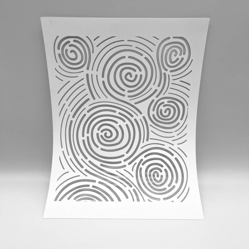 Op de afbeelding: Witte papieren uitsnede met een patroon van concentrische cirkels en gebogen lijnen. Het ontwerp cre&euml;ert een wervelend, abstract effect. Het papier is licht gebogen, wat diepte aan het kunstwerk toevoegt. De algehele esthetiek is minimalistisch en modern.