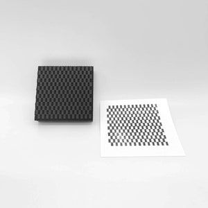 May include: A black and white checkered pattern printed on a piece of paper and a black foam block with the same pattern.