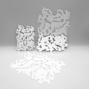 May include: Three white, abstract, laser-cut shapes of varying sizes. The shapes have an organic, irregular pattern with negative space, resembling a stylized landscape or cellular structure. The pieces are arranged on a light grey surface.