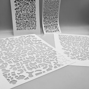 May include: Four white paper stencils with intricate, abstract cut-out designs. The stencils vary in size and shape, with some curved and others flat. The cut-out patterns are complex and detailed, creating negative space designs.