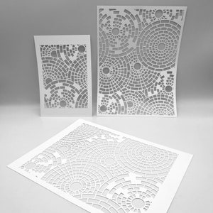 Puede incluir: Tres plantillas de papel blanco con un patrón geométrico de círculos superpuestos. Las plantillas están recortadas para crear un diseño de círculos dentro de círculos.