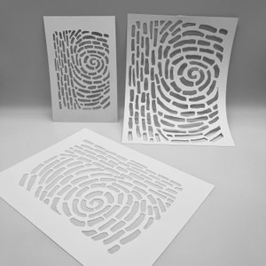 May include: Three white stencils with a fingerprint design. Each stencil features a unique arrangement of cut-out shapes, creating a textured pattern. The stencils vary in size and are arranged on a light grey surface.