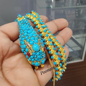 Può includere: Una collana a forma di serpente in oro e turchese con una catena e una chiusura. La collana è decorata con pietre turchesi e dettagli rossi e bianchi. Il testo "Poonam Art Jewels" è visibile nell'immagine.