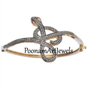 Pode incluir: Um bracelete de cobra de prata com um design incrustado de diamantes. A cobra está enroscada com a cabeça voltada para a frente. O bracelete é feito de ouro e prata e tem um acabamento polido. O bracelete é adornado com pequenos diamantes brilhantes.