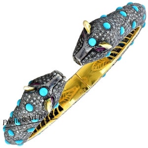 May include: A gold and silver bracelet with two snake heads, set with turquoise and diamonds. The bracelet is decorated with black diamonds and turquoise stones.