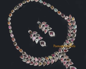 May include: A silver necklace and earrings set with a cascading design of multi-colored gemstones. The necklace features a row of oval-shaped gemstones and a pendant with a teardrop-shaped gemstone. The earrings have a similar cascading design with teardrop-shaped gemstones.