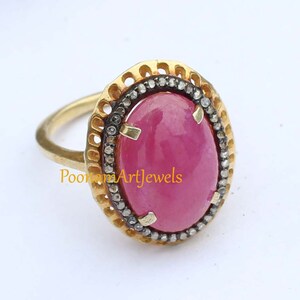 Puede incluir: Un anillo de oro con una gran piedra ovalada rosa rodeada por un halo de diamantes más pequeños. El anillo tiene un diseño delicado e intrincado.