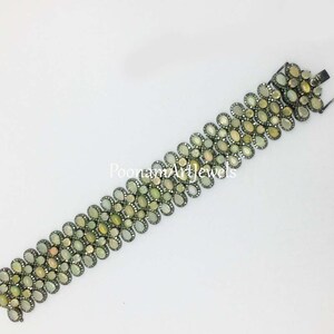 May include: A silver bracelet with a row of oval-shaped green gemstones and smaller round diamonds. The bracelet has a clasp closure.