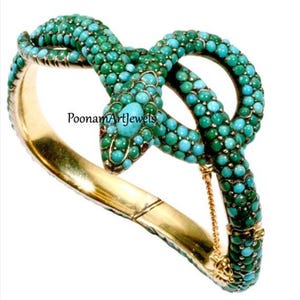 May include: A gold bangle bracelet with a turquoise and green snake design. The snake is coiled around the bracelet and has a ruby eye. The bracelet is hinged and has a chain closure.