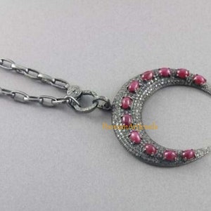 Puede incluir: Un collar con un colgante de media luna de plata. El colgante está engastado con rubíes rojos y pequeños diamantes.