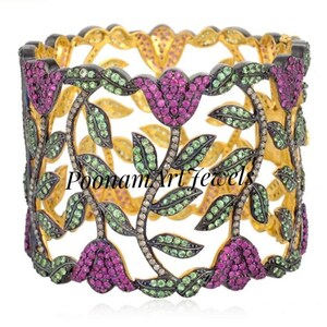Peut inclure: Un bracelet jonc en or avec un motif floral. Le bracelet est serti de pierres précieuses roses, vertes et blanches. Le bracelet est ouvert et a une bande large et plate.