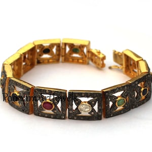 May include: Gold-toned bracelet with square links, each featuring a central gemstone and surrounding diamond accents. Gemstones include ruby, emerald, and sapphire. The bracelet is open, showing the clasp and the Poonam Artjewels logo.