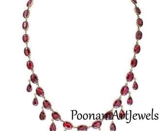Puede incluir: Un collar de oro con una fila de piedras preciosas rojas de forma ovalada y una fila de piedras preciosas rojas en forma de lágrima que cuelgan. El collar está etiquetado como "PoomamArtjewels".
