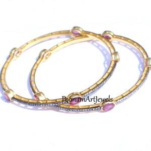 Könnte beinhalten: Zwei goldene Armreifen mit einer Reihe kleiner Diamanten und rosafarbenen ovalen Edelsteinen. Die Armreifen liegen übereinander. Der Text "PoonamArtJewels" ist auf dem unteren Armreif sichtbar.