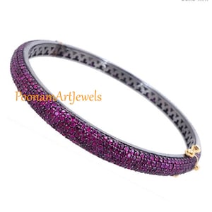 May include: A silver bangle bracelet with a row of small, pink gemstones. The bracelet is open and has a hinged clasp.