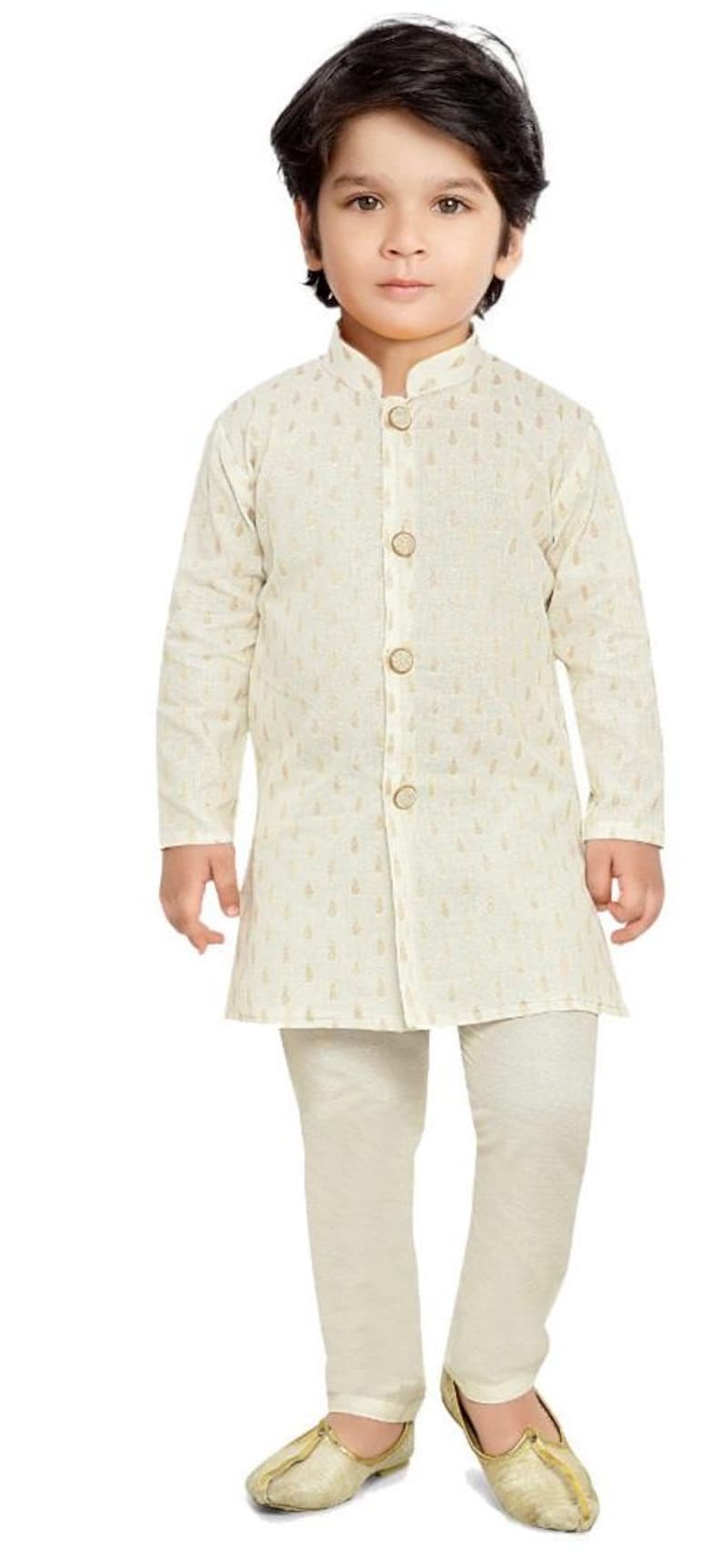May include: A young boy wearing a white kurta with gold embroidery and matching white trousers. He is wearing gold shoes.