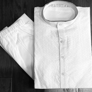 May include: White cotton kurta pajama set with a button-up front and a mandarin collar. The kurta has a subtle geometric pattern.