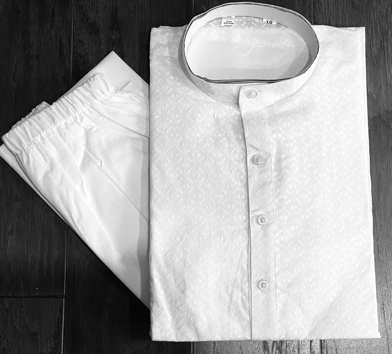 May include: White cotton kurta pajama set with a button-up front and a mandarin collar. The kurta has a subtle geometric pattern.